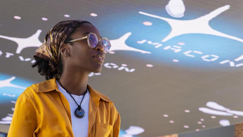 Young woman standing under a digital art display.